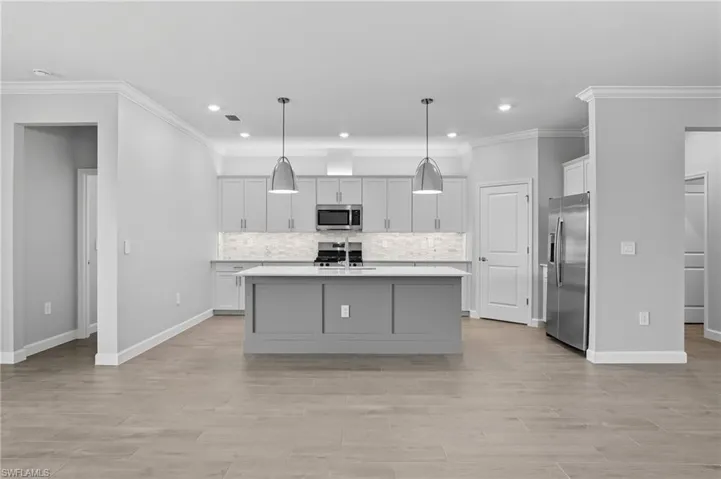 Kitchen featuring ornamental molding, pendant lighting, a kitchen island with sink, stainless steel appliances, and gray cabinetry