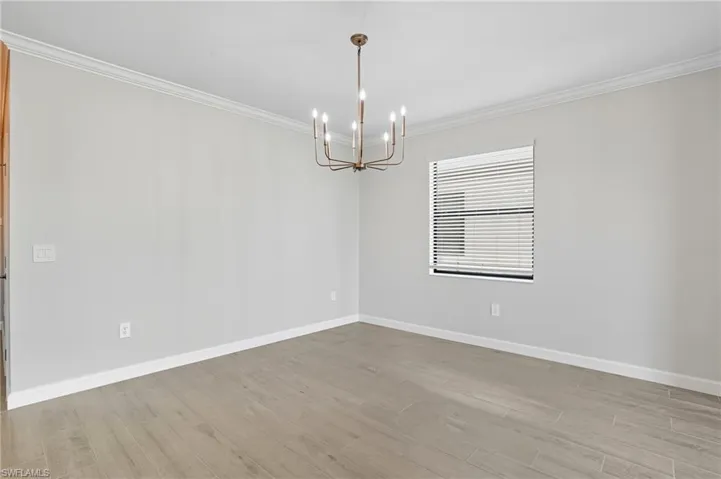 Spare room with crown molding, light wood-style floors, and a chandelier