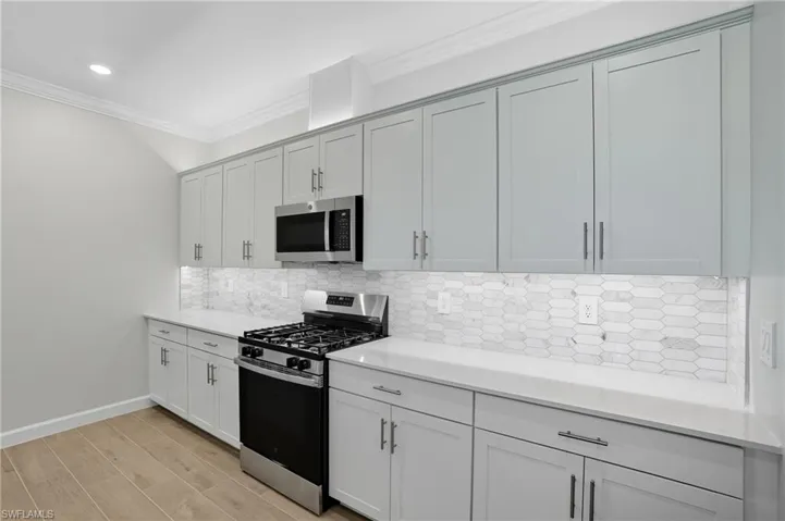 Kitchen featuring stainless steel appliances, tasteful backsplash, crown molding, light stone counters, and light wood-type flooring
