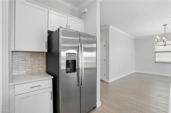 Kitchen with stainless steel refrigerator with ice dispenser, ornamental molding, white cabinetry, light wood-type flooring, and tasteful backsplash