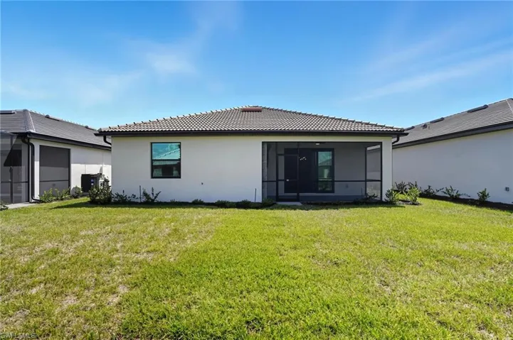 Back of house with a sunroom, a lawn, a tiled roof, and stucco siding