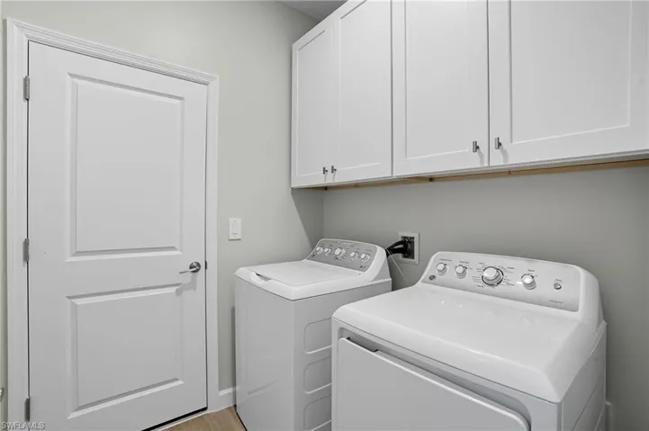 Laundry room with independent washer and dryer, cabinet space, and light wood-style flooring