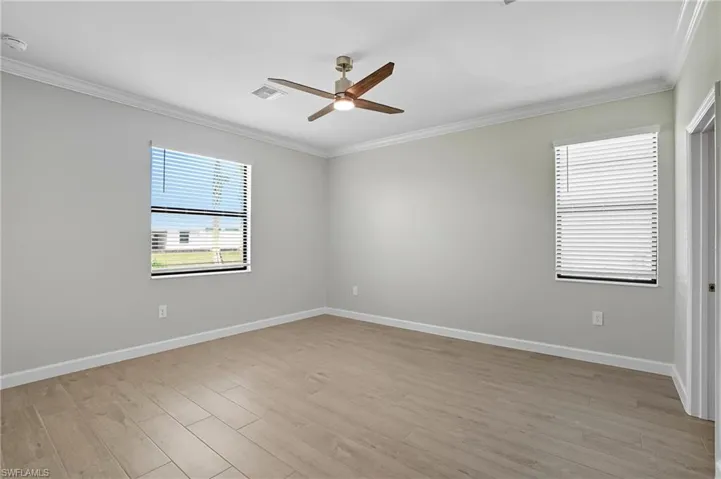 Empty room with ornamental molding, light wood-type flooring, healthy amount of natural light, and ceiling fan