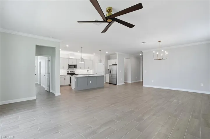 Unfurnished living room with a ceiling fan, ornamental molding, light wood-style floors, recessed lighting, and a chandelier