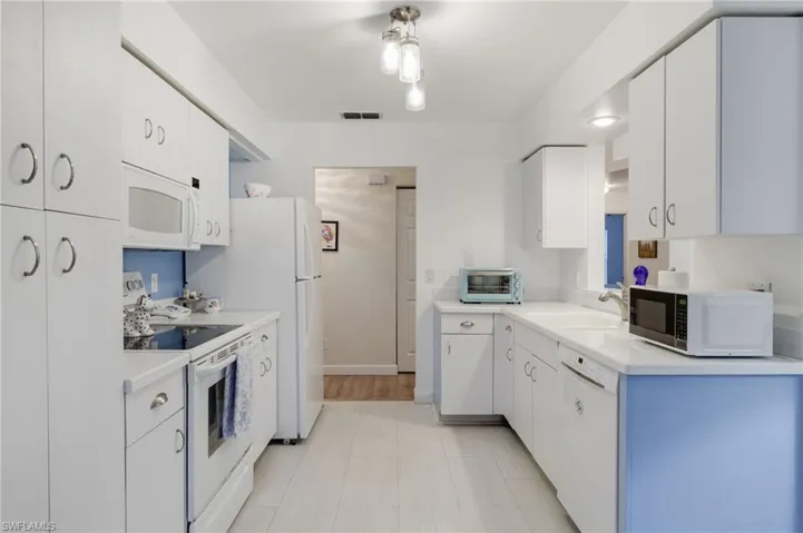 Kitchen with light flooring, white appliances, and white cabinetry