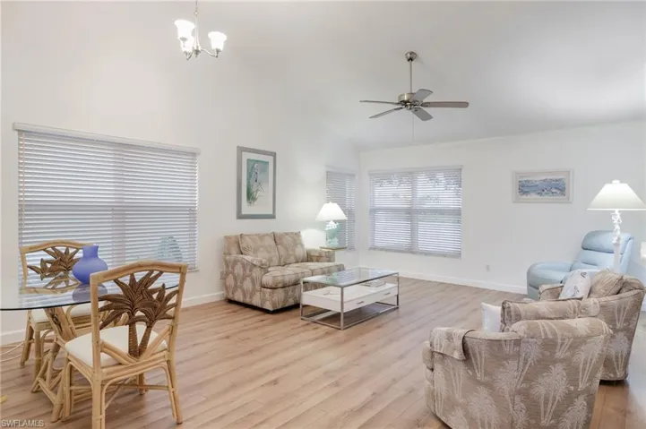 Living room featuring high vaulted ceiling, wood-style flooring, and ceiling fan with notable chandelier
