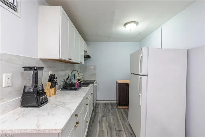 Unit A)Kitchen with freestanding refrigerator, range with electric stovetop, decorative backsplash, wood tiled floors, and white cabinets