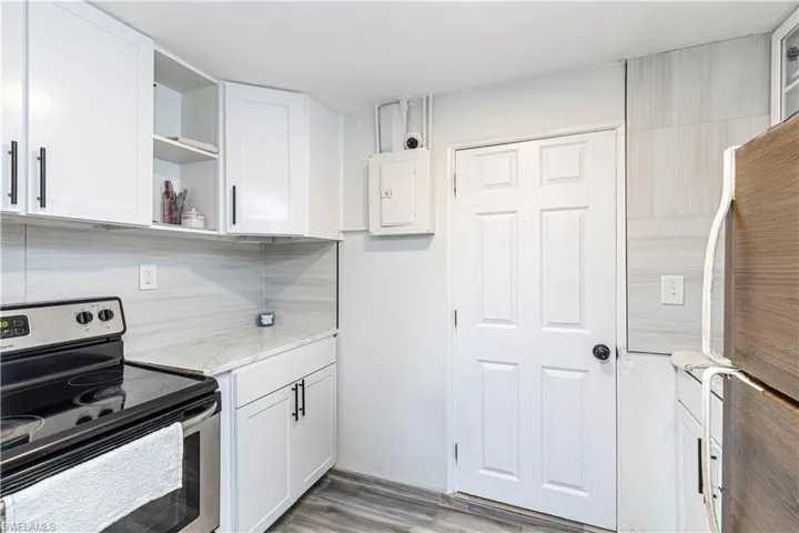 Unit B)Kitchen featuring stainless steel electric range oven, open shelves, freestanding refrigerator, white cabinetry, and electric panel