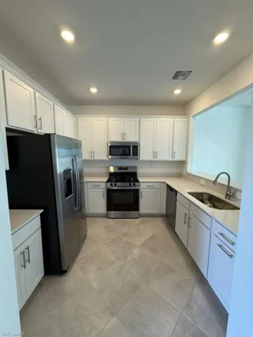 Kitchen with stainless steel appliances, white cabinets, recessed lighting, and light stone countertops