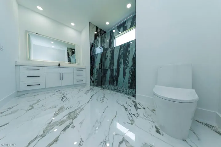 Full bathroom with a marble finish shower, baseboards, toilet, recessed lighting, and vanity