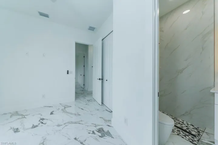 Bathroom with marble finish floors, baseboards, toilet, and a marble finish shower
