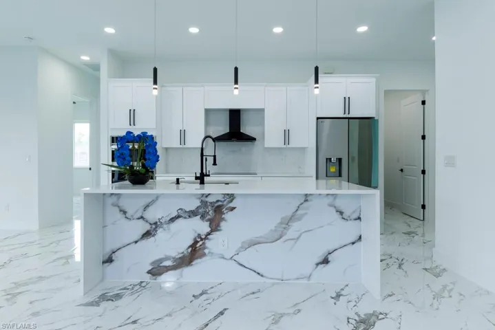 Kitchen featuring stainless steel refrigerator with ice dispenser, an island with sink, wall chimney exhaust hood, white cabinets, and recessed lighting
