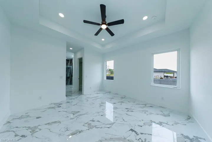 Empty room featuring a tray ceiling, recessed lighting, baseboards, ceiling fan, and marble finish floors