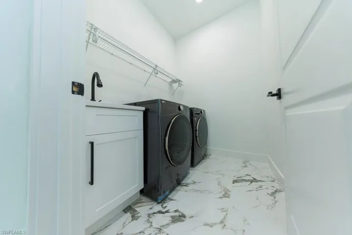 Washroom featuring washer and dryer, light marble finish floors, and baseboards