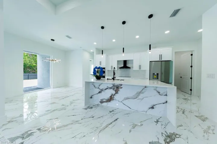 Kitchen with stainless steel fridge, wall chimney exhaust hood, a sink, white cabinets, and a large island with sink