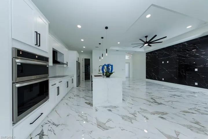 Kitchen with stainless steel double oven, wall chimney exhaust hood, recessed lighting, black electric cooktop, and white cabinetry