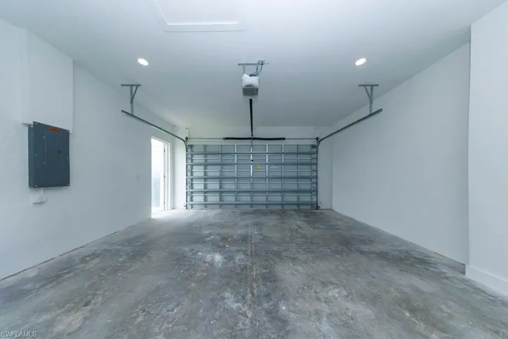 Garage with electric panel, a garage door opener, and recessed lighting