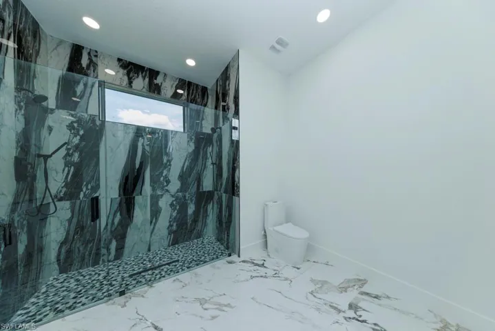 Bathroom with toilet, recessed lighting, marble finish flooring, a marble finish shower, and baseboards