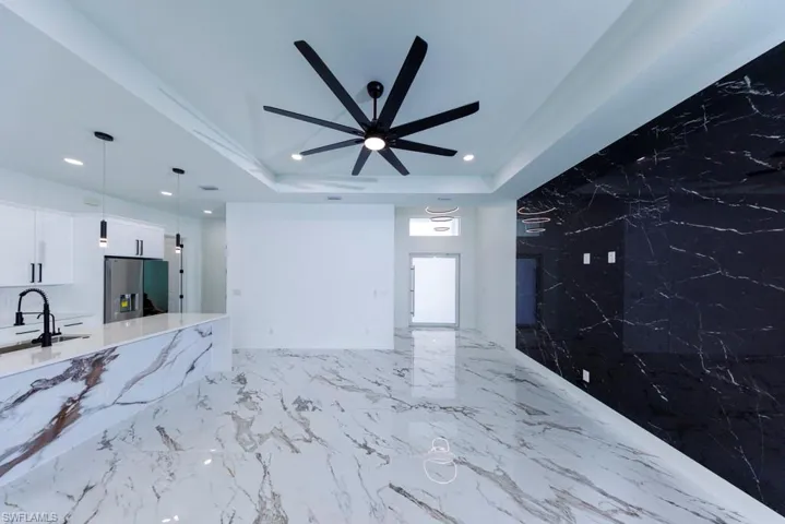 Unfurnished living room with recessed lighting, a ceiling fan, a tray ceiling, and a sink