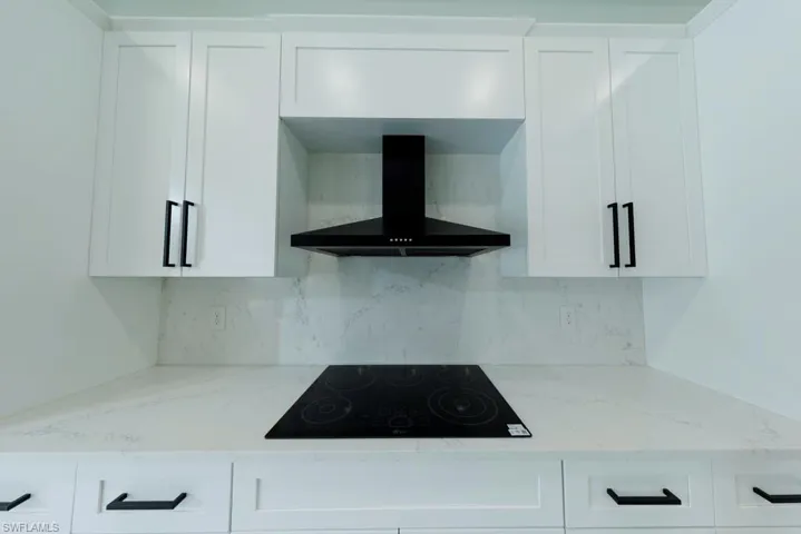 Kitchen featuring wall chimney exhaust hood, black electric stovetop, white cabinets, and tasteful backsplash