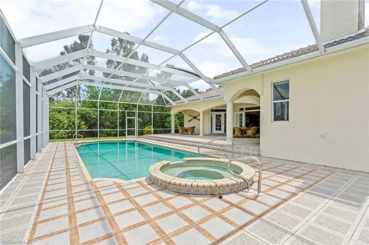 View of swimming pool featuring a patio area, a pool with connected hot tub, and glass enclosure