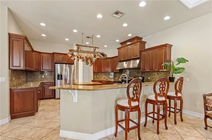 Kitchen featuring stainless steel appliances, under cabinet range hood, a peninsula, light stone counters, and tasteful backsplash