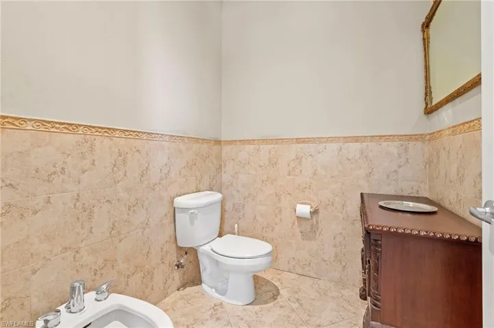 Half bathroom featuring tile walls, a bidet, and a wainscoted wall