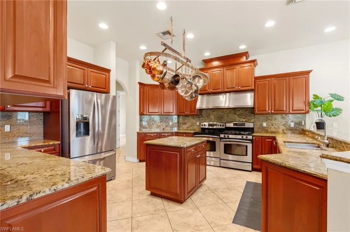 Kitchen with wall chimney range hood, appliances with stainless steel finishes, light stone countertops, tasteful backsplash, and arched walkways