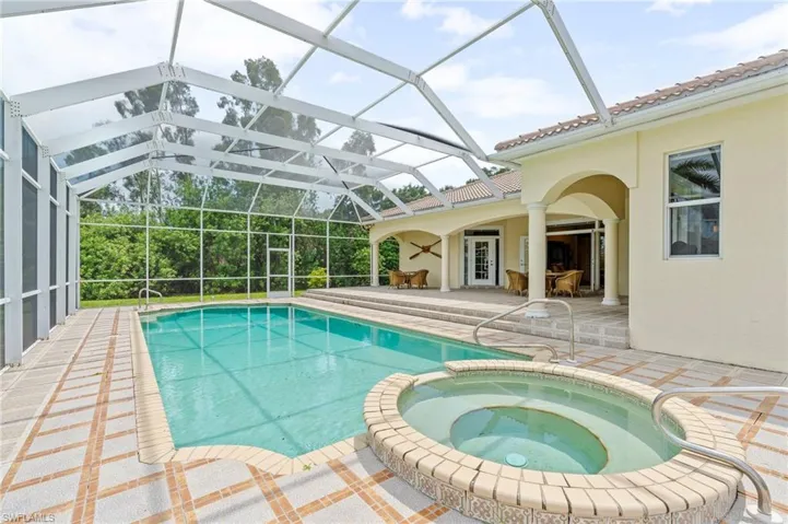 View of swimming pool with a patio area, a pool with connected hot tub, and glass enclosure