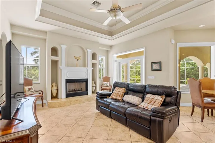 Living area featuring light tile patterned flooring, a tray ceiling, a fireplace with raised hearth, ceiling fan, and ornamental molding