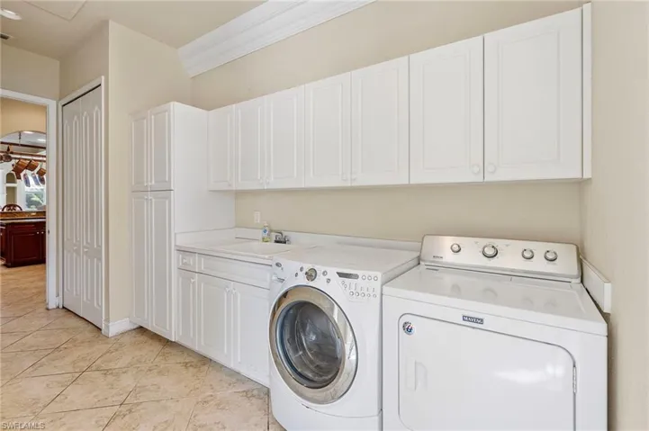 Laundry area featuring cabinet space, washer and dryer, ornamental molding, and light tile patterned flooring