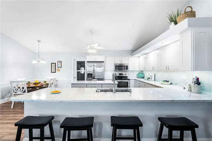 Kitchen with decorative backsplash, appliances with stainless steel finishes, white cabinets, a sink, and a peninsula