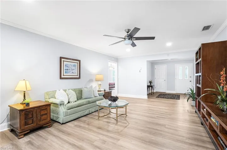 Living area with a ceiling fan, baseboards, visible vents, light wood-type flooring, and crown molding