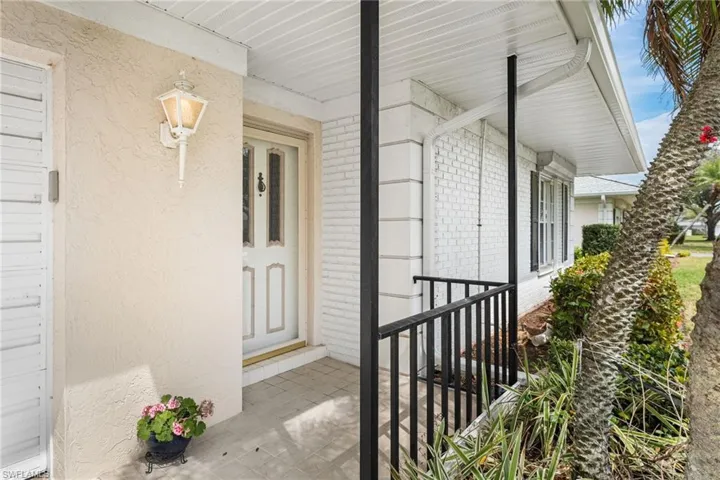 Doorway to property featuring covered porch, stucco siding, and brick siding
