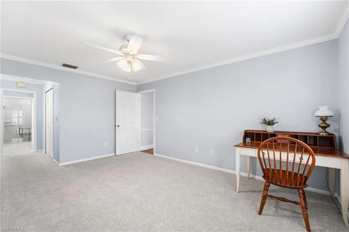 Office space with carpet floors, a ceiling fan, visible vents, baseboards, and crown molding
