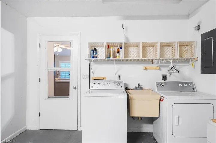 Laundry area with laundry area, a sink, baseboards, electric panel, and washer and clothes dryer