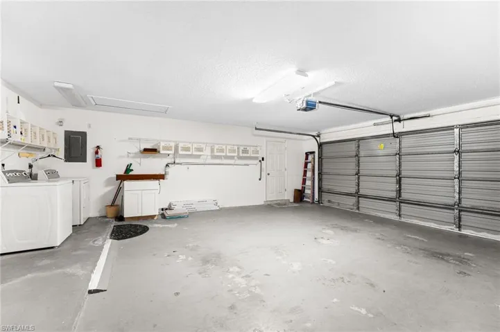 Garage with separate washer and dryer, electric panel, and a garage door opener