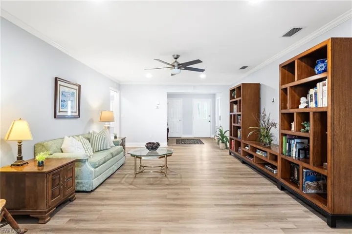 Living area featuring visible vents, ornamental molding, a ceiling fan, light wood-type flooring, and baseboards