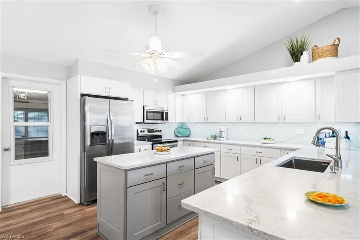 Kitchen featuring light stone counters, lofted ceiling, gray cabinets, appliances with stainless steel finishes, and a sink