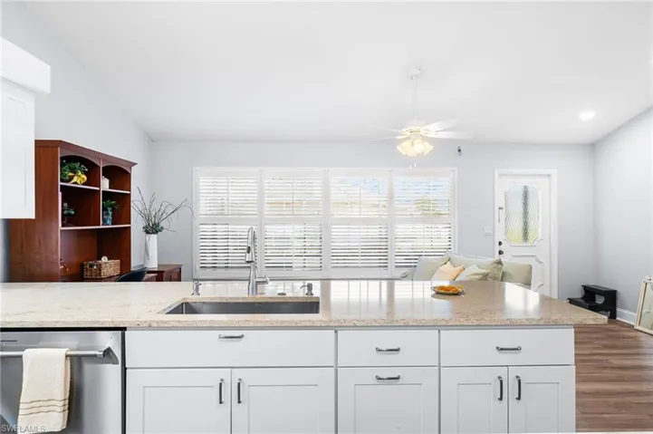 Kitchen with white cabinets, dishwasher, dark wood-style flooring, light stone countertops, and a sink