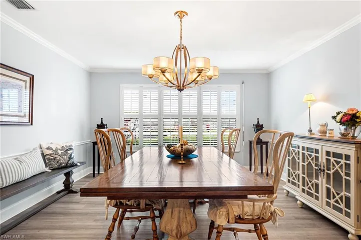 Dining area with ornamental molding, visible vents, light wood finished floors, and an inviting chandelier