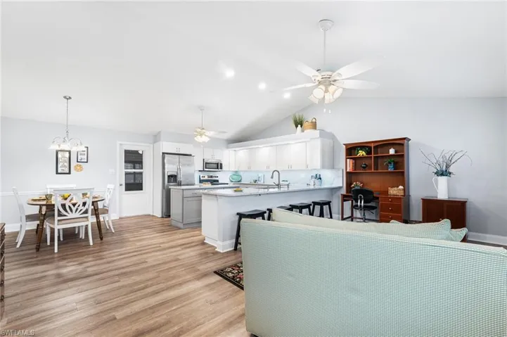 Living area featuring recessed lighting, lofted ceiling, light wood-type flooring, baseboards, and ceiling fan with notable chandelier
