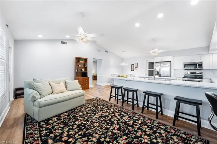 Living area featuring lofted ceiling, light wood-style flooring, visible vents, and ceiling fan with notable chandelier