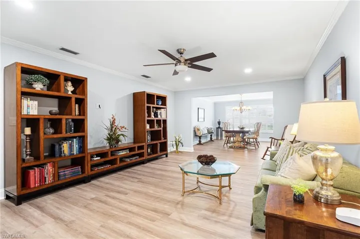 Living room featuring crown molding, visible vents, wood finished floors, and ceiling fan with notable chandelier