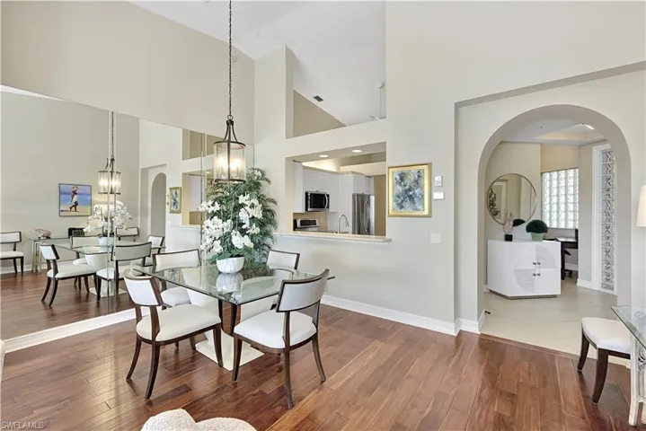High-ceiling interior featuring wood-finish flooring, a wall-mounted mirror, an arched entryway, and a pass-through opening to the kitchen area