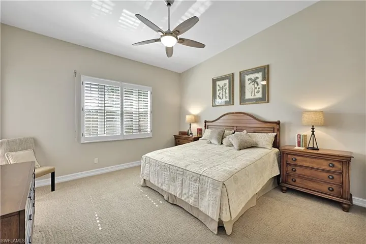 Vaulted ceiling with a central brushed metal ceiling fan, neutral wall tones, and plantation shutter window treatments