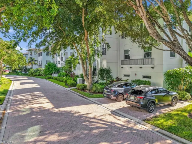 Multi-story residence featuring stucco exterior, second-level balcony with metal railing, brick-paver driveway, and mature landscaping
