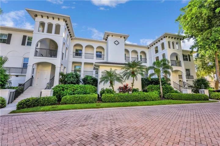 Mediterranean-inspired architectural exterior featuring stucco siding, arched loggias, ornate metal railings, and a herringbone-patterned brick driveway