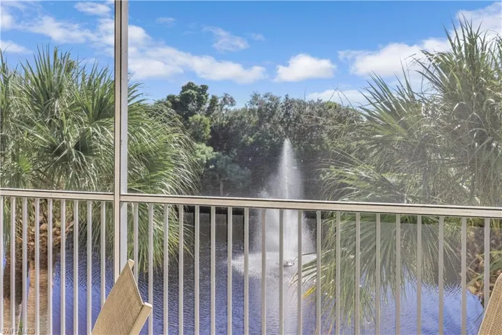 Screened-in balcony featuring vertical metal railing, overlooking a pond with an active water fountain and mature palm trees