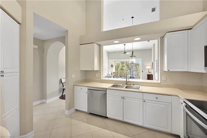 Kitchen featuring white cabinetry, stainless steel appliances, neutral solid-surface countertops, tile flooring, and a pass-through window beneath a high vaulted ceiling
